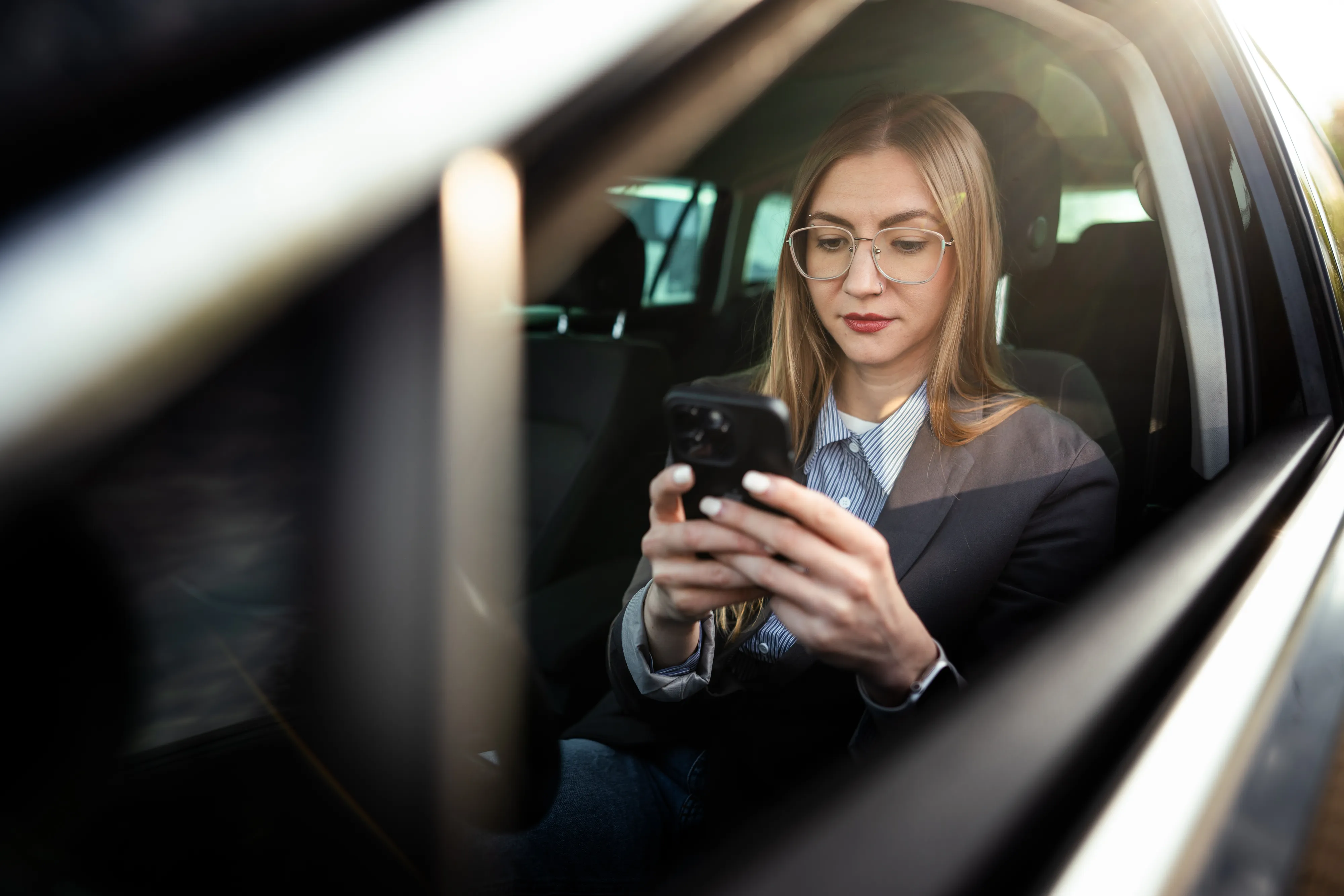 A woman in glasses looking at her phone in a car